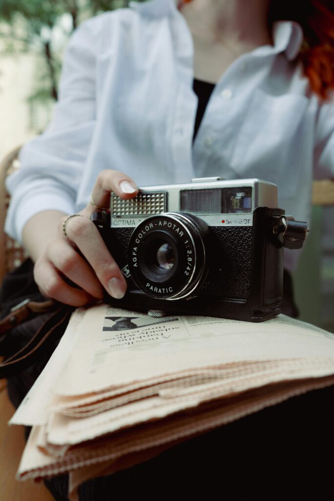 A woman holding a camera and reading a newspaper